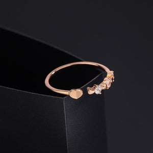 A close-up image of a woman's hand wearing a dainty heart-shaped stacking ring with gold plating on the finger.