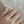 Rose gold ring with a diamond on a person's finger against a neutral background