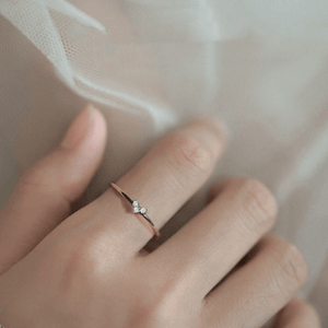 Rose gold ring with a diamond on a person's finger against a neutral background