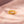 Gold ring with intricate design on a soft pink fabric background