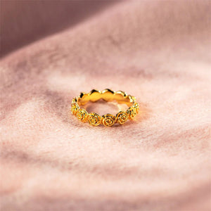 Gold ring with intricate design on a soft pink fabric background