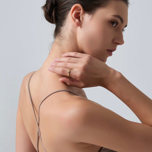 Woman with a gold ring on her hand touching her neck against a light gray background