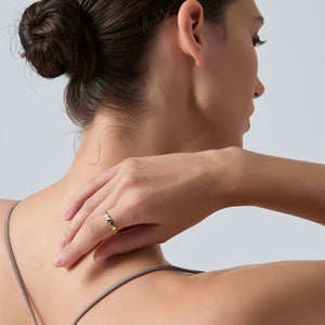 Woman with a gold ring on her finger touching her neck against a light gray background