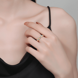Close-up of a hand wearing a gold ring with gemstones, against a neutral background.