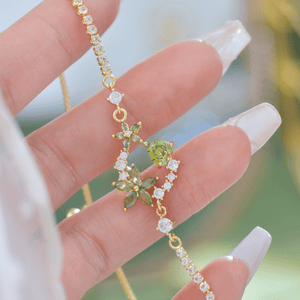 Gold necklace with green gemstones held by a hand against a blurred background