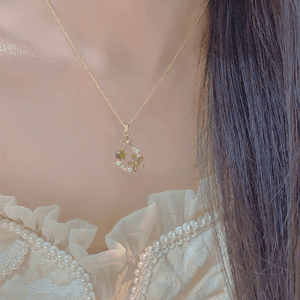 Gold necklace with a delicate pendant worn by a person with light-colored hair.