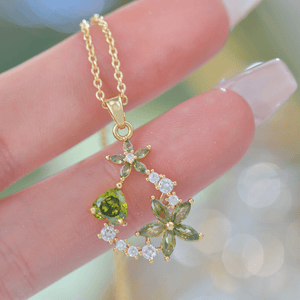 Gold necklace with green gemstones held by a hand against a blurred background