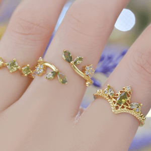 Gold ring with green gemstones on a finger against a blurred background
