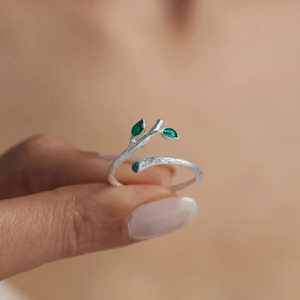 Silver ring with green gemstones on a finger against a blurred background