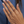Hand wearing two delicate rings with green gemstones against a blue background