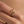 Gold ring with green gemstones on a finger against a beige background