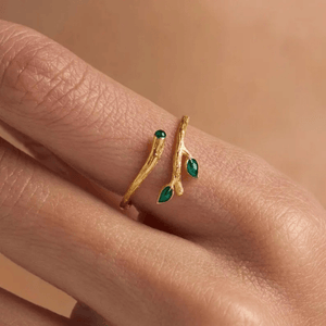 Gold ring with green gemstones on a finger against a beige background