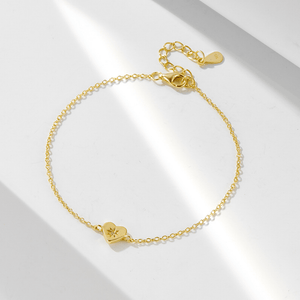 Gold bracelet with heart charm on a light gray background