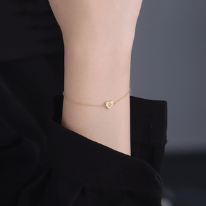 Gold bracelet with a heart charm on a wrist against a dark background