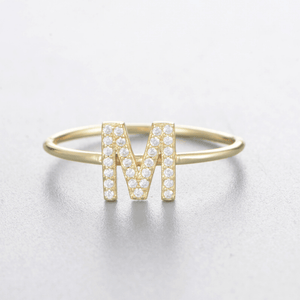Gold ring with letter 'M' design on a light gray background