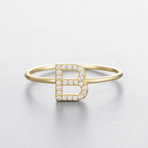 Gold ring with letter 'B' and diamonds on a light gray background