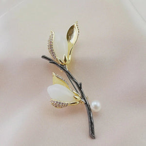 Gold and black leaf-shaped brooch with pearls on a beige background