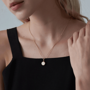 A woman wearing a gold necklace with a round opal locket on a light gray background