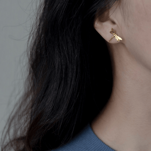 Gold dragonfly earring worn by a person with dark hair against a neutral background