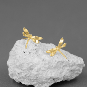 Gold dragonfly earrings on a gray stone surface