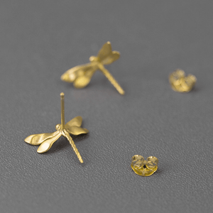 Gold dragonfly-shaped earrings on a gray background