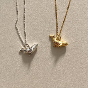 Gold and silver whale-shaped pendants on chains against a beige background