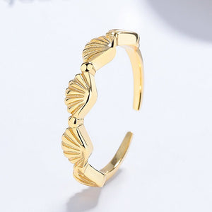Gold open ring with shell-like design on a light gray background