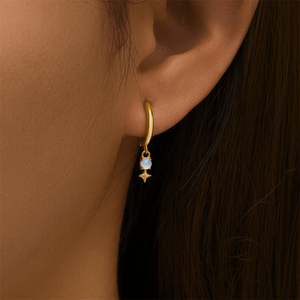 Gold earring with a blue gemstone worn by a person with dark hair.