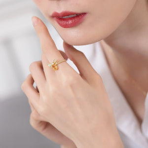 Close-up of a hand wearing a gold ring with a butterfly design, against a neutral background.