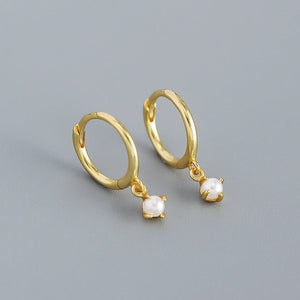 Gold hoop earrings with pearl drops on a gray background