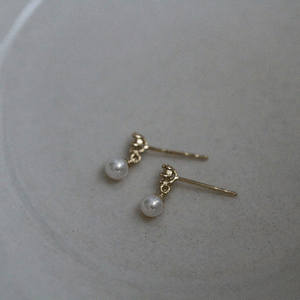 Pair of gold earrings with pearl drops on a light gray background