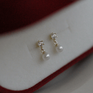 Pair of pearl earrings with gold accents on a soft fabric background
