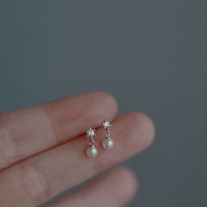 Pearl and diamond earrings held between fingers against a neutral background