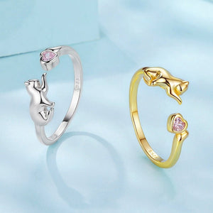 Two cat-shaped rings, one silver and one gold, on a light blue background.
