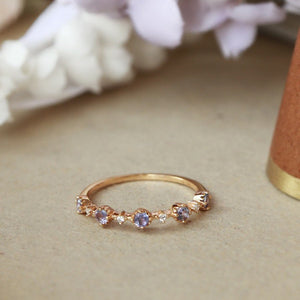 Gold ring with purple gemstones on a beige surface with flowers in the background
