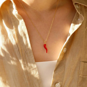 Person wearing a gold necklace with a red chili pepper pendant.