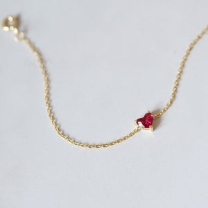 Gold necklace with a red heart-shaped gemstone on a light gray background
