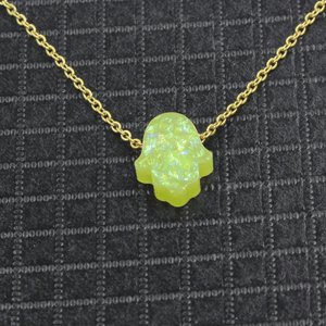 Neon green opal hamsa pendant on a gold chain against a dark textured background