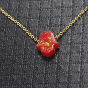 Red Hamsa hand pendant necklace on a gold chain against a textured gray background