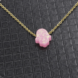 Pink glittery Hamsa hand necklace on a gold chain against a dark textured background