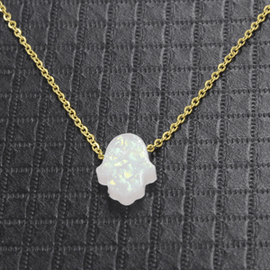 Necklace with a white opal hamsa pendant on a gold chain against a gray textured background