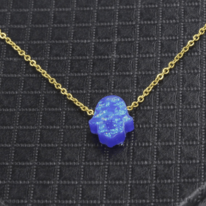 Blue Hamsa pendant on a gold chain against a black textured background