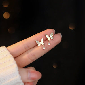 Butterfly-shaped earrings with gemstones held in a hand against a dark background