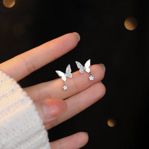 Butterfly-shaped earrings on a hand against a dark background
