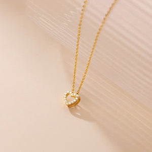 Gold necklace with a heart-shaped pendant on a beige background