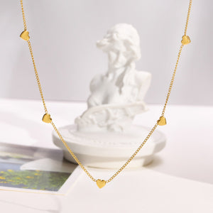 Gold necklace with heart-shaped pendants on a white surface with a marble bust in the background