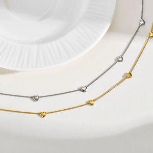 Two layered heart-shaped necklace chains, one gold and one silver, on a white background.
