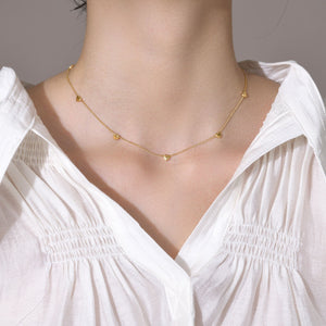 Gold necklace on a person wearing a white blouse against a neutral background