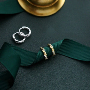 Two pairs of earrings on a dark surface with green ribbons.