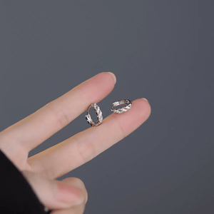 Two silver hoop earrings held between fingers against a dark background